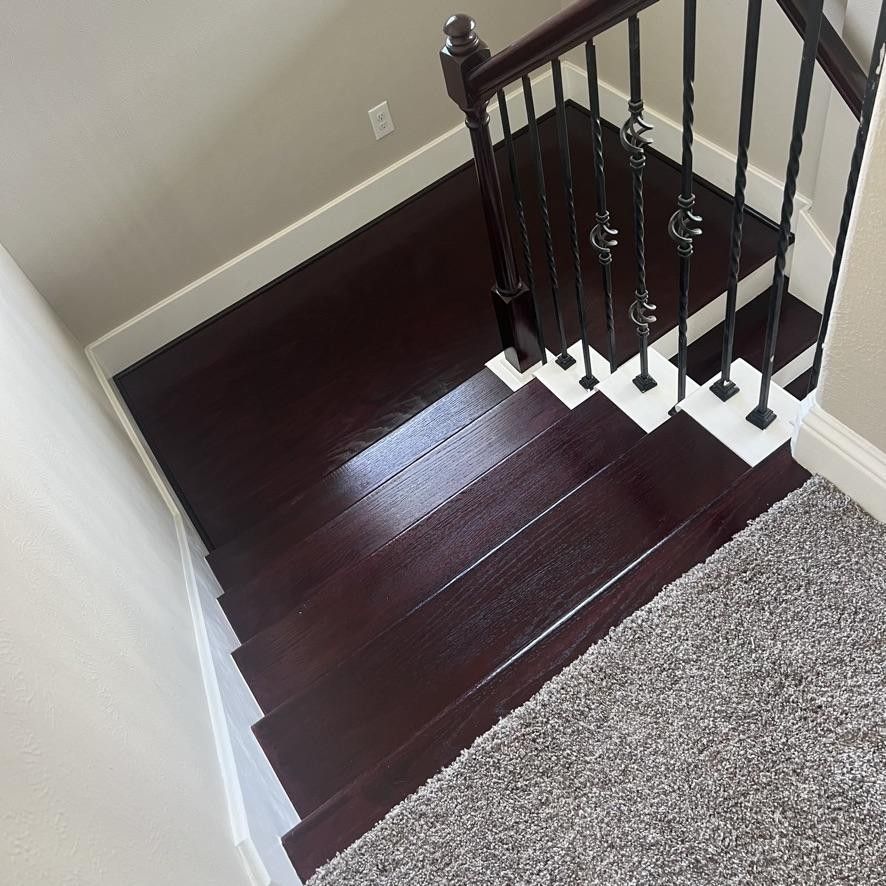 Dark wooden staircase with black metal railing beside a carpeted landing and white wall.