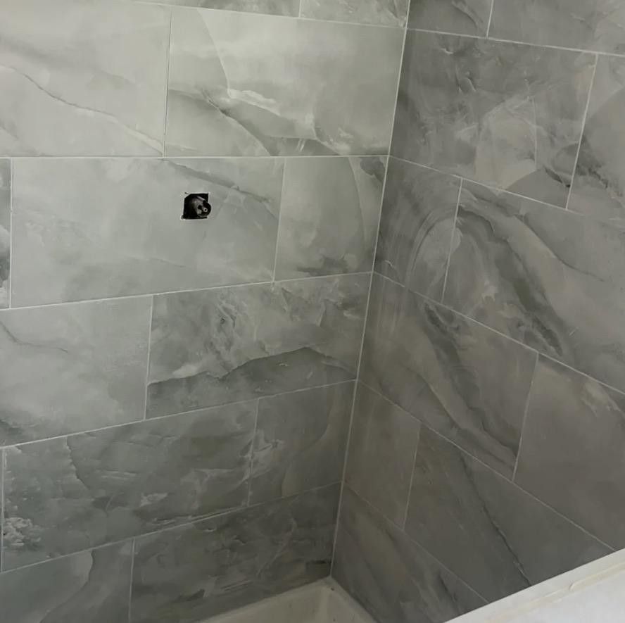 Empty tiled shower corner with gray marble-look walls and a small pipe opening.