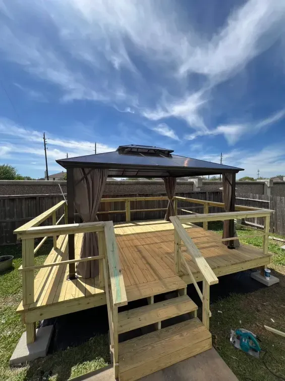 Wooden backyard deck with railings and a gazebo under a bright blue sky