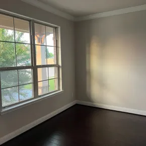 Empty room with dark wood floor, gray walls, and a large sunlit window.