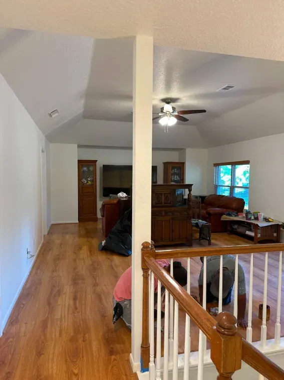 Interior hallway opening into a living room with wood floors, ceiling fan, and wooden furniture