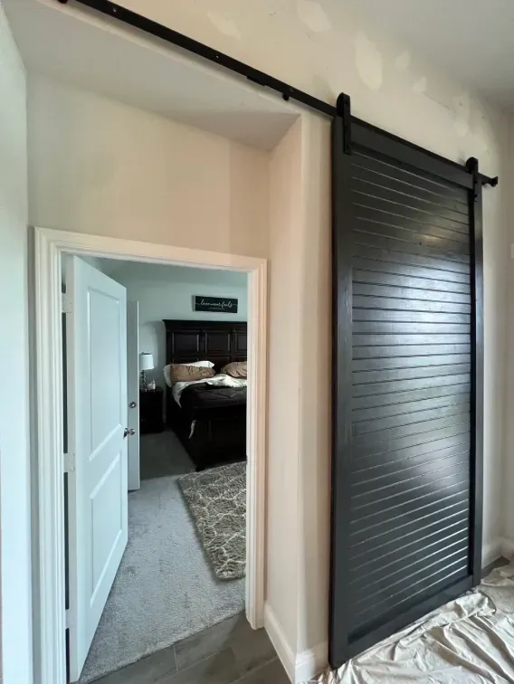 Interior doorway with a black barn door, opening into a gray-carpeted bedroom.