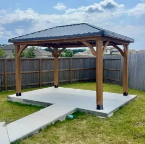 Wooden pavilion with metal roof on a concrete patio in a fenced backyard