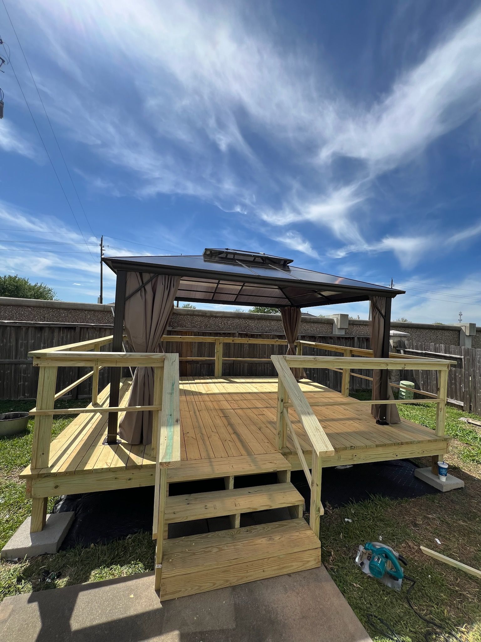 Wooden backyard deck with railings and steps under a partly cloudy blue sky