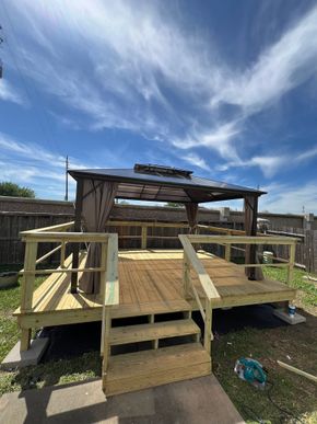 Wooden backyard deck with railings and steps under a partly cloudy blue sky