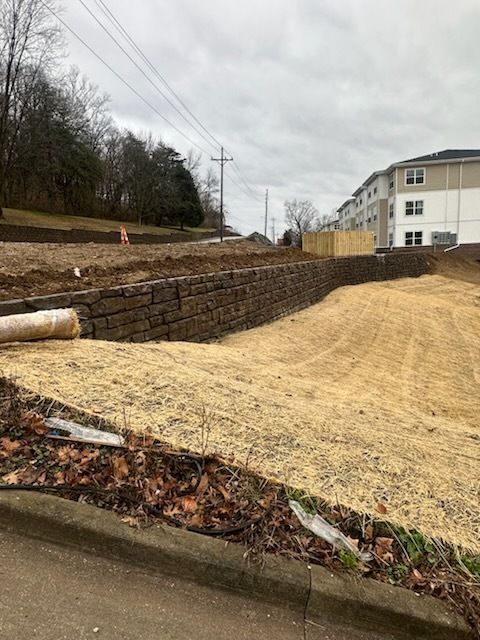 A brick wall is surrounding a dirt field with a building in the background.