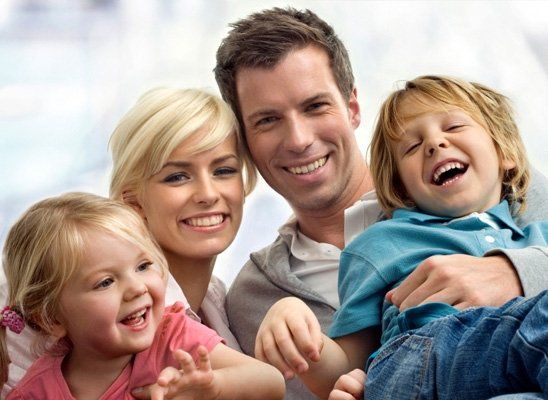 A cheerful family of four smiling and laughing together in a bright, indoor setting.