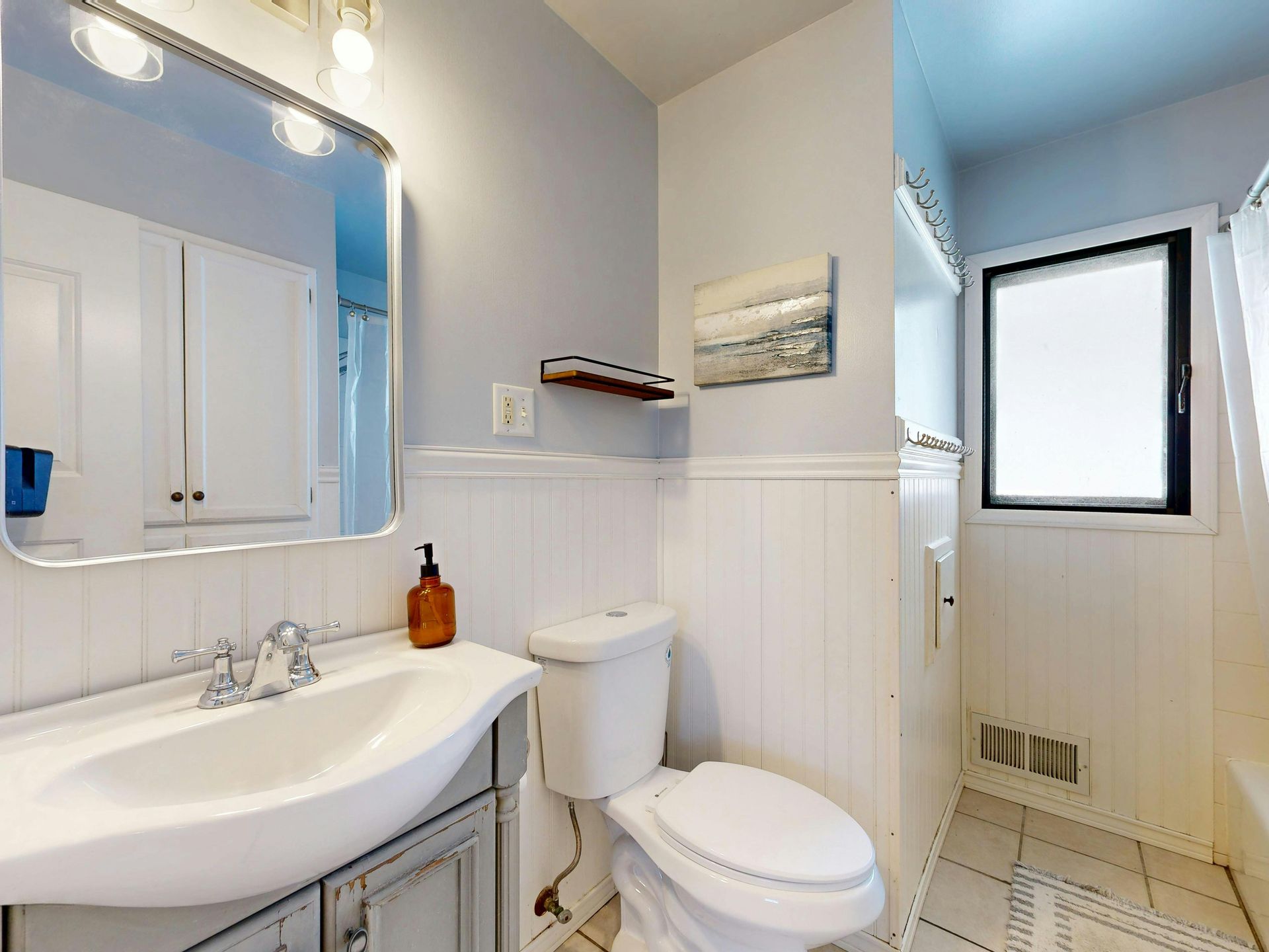 Bathroom with a white sink, toilet, and walls. A mirror and window are also visible.