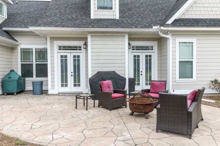 Patio with wicker chairs and coffee table outside a gray house with French doors.