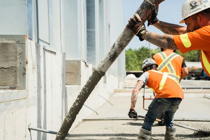 Construction workers in orange vests pouring concrete with a hose outside a building