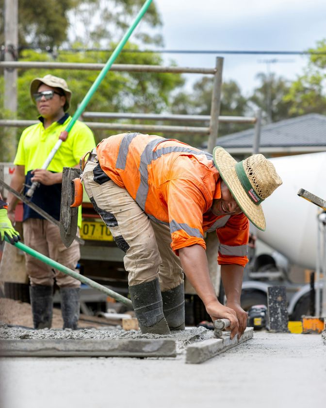 Construction worker in orange vest smoothing wet concrete at a worksite