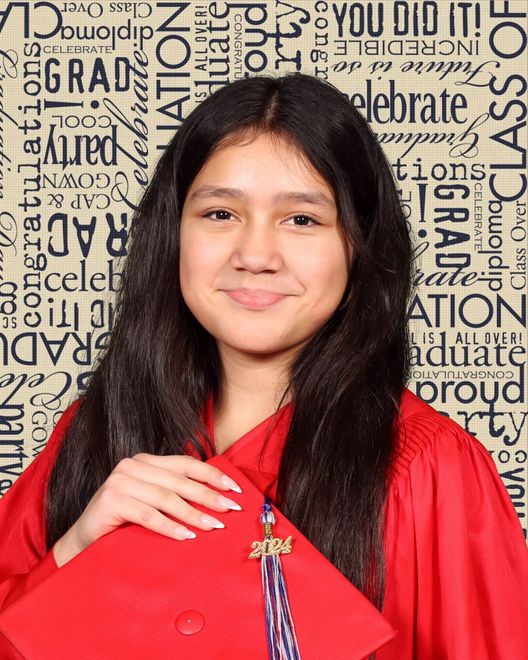 A young girl in a red graduation cap and gown is smiling.