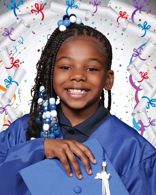 A young girl in a graduation cap and gown is smiling