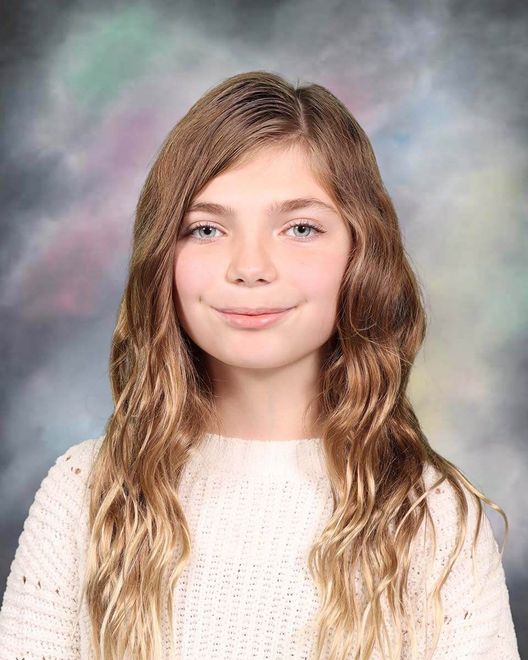 The girl is wearing a white sweater and smiling for the camera.