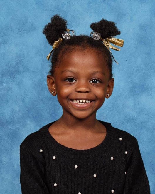 A little girl in a black sweater is smiling for the camera