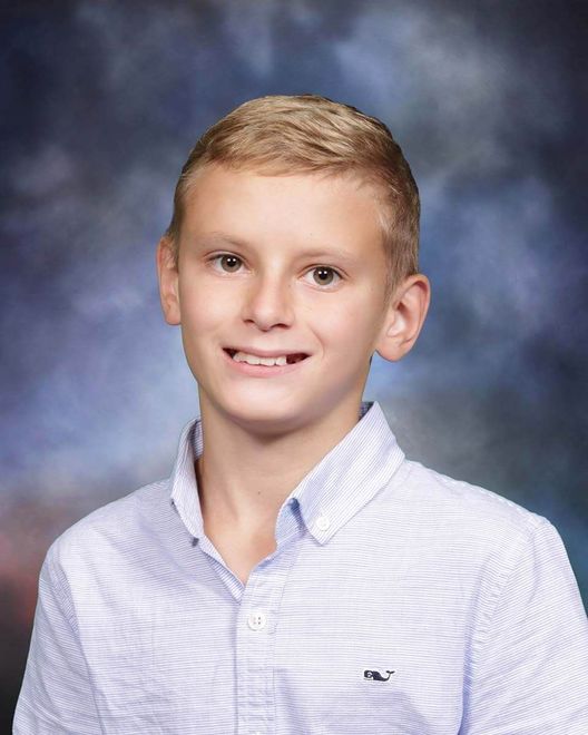 A young boy in a blue and white striped shirt is smiling for a picture.