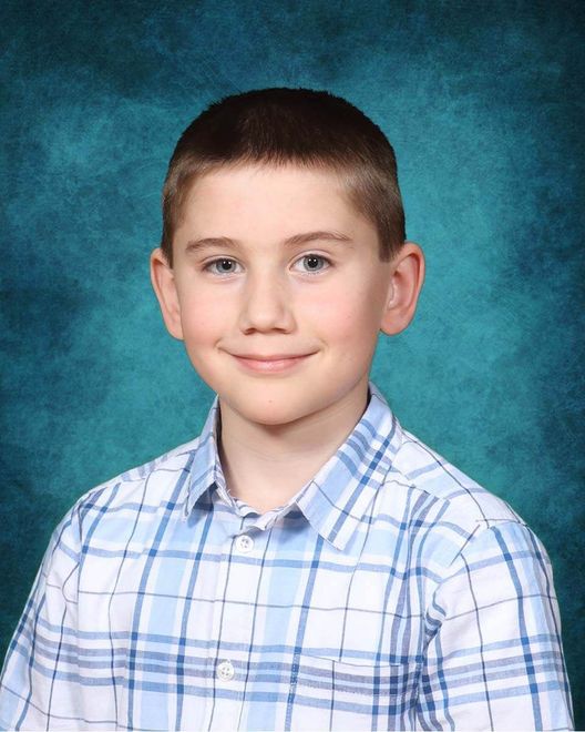 A young boy in a plaid shirt is smiling for the camera.