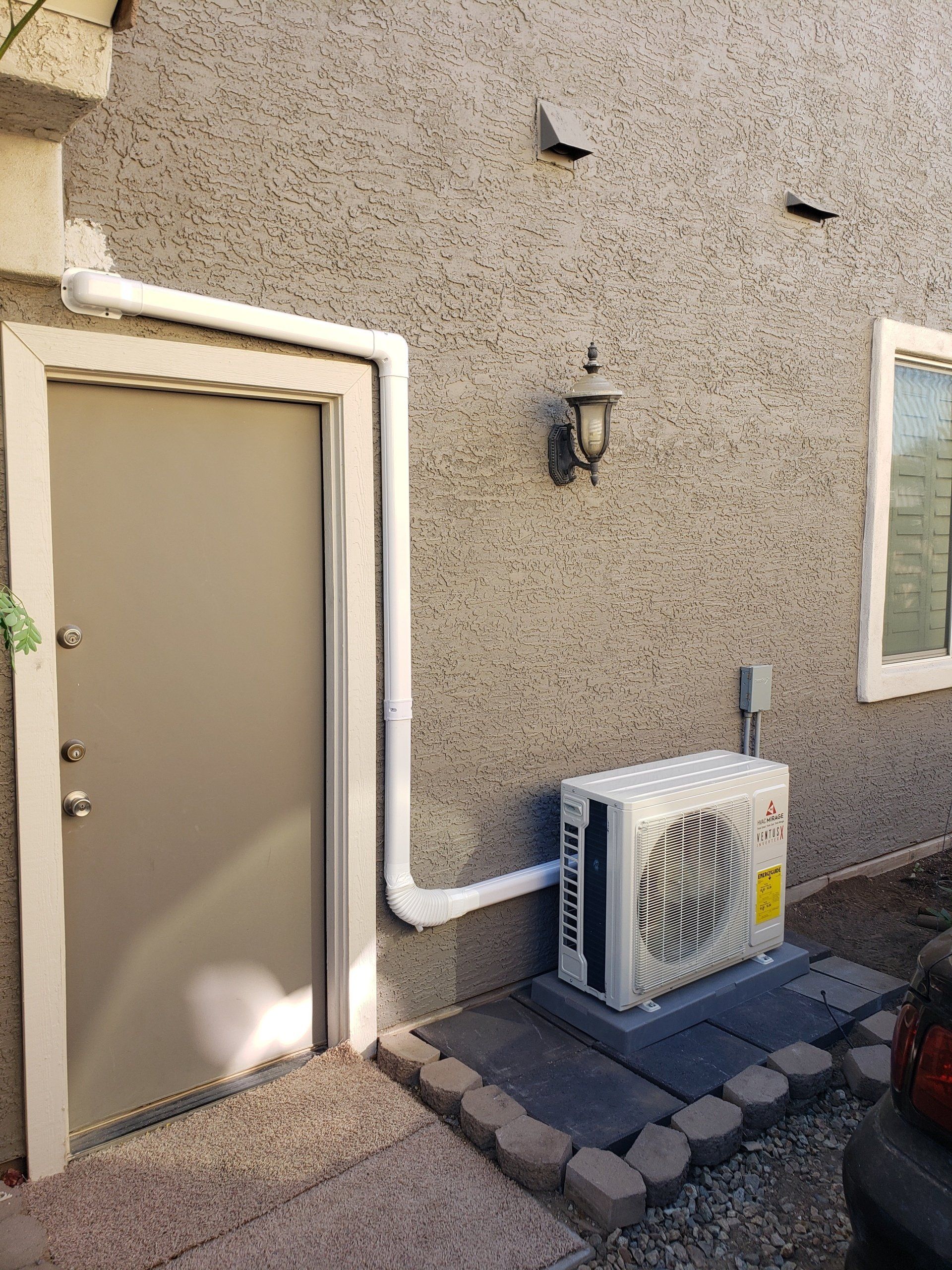 White air conditioning unit outside a stucco building, beside a door.