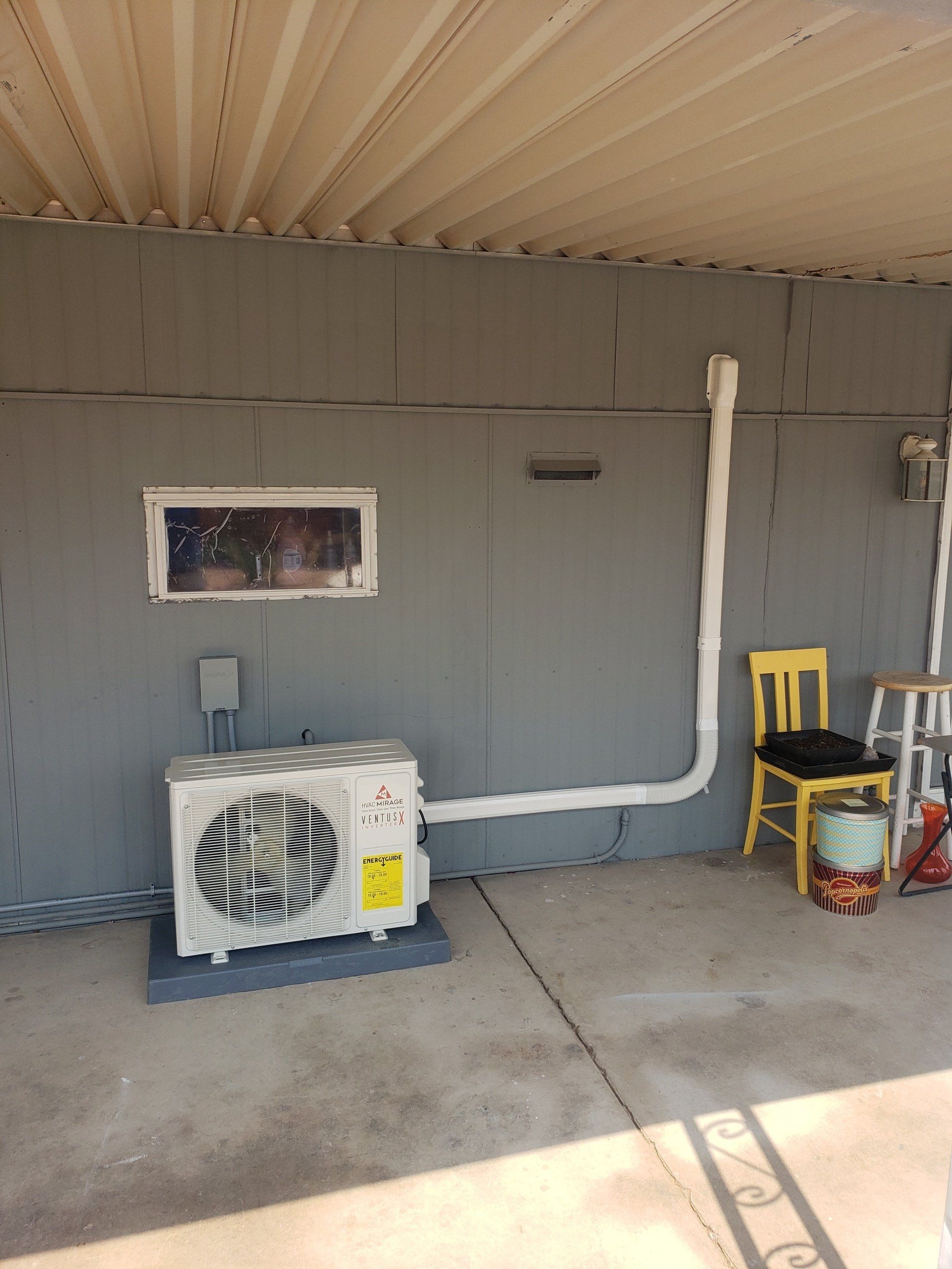 An outdoor air conditioning unit with a white exhaust pipe on a gray wall.