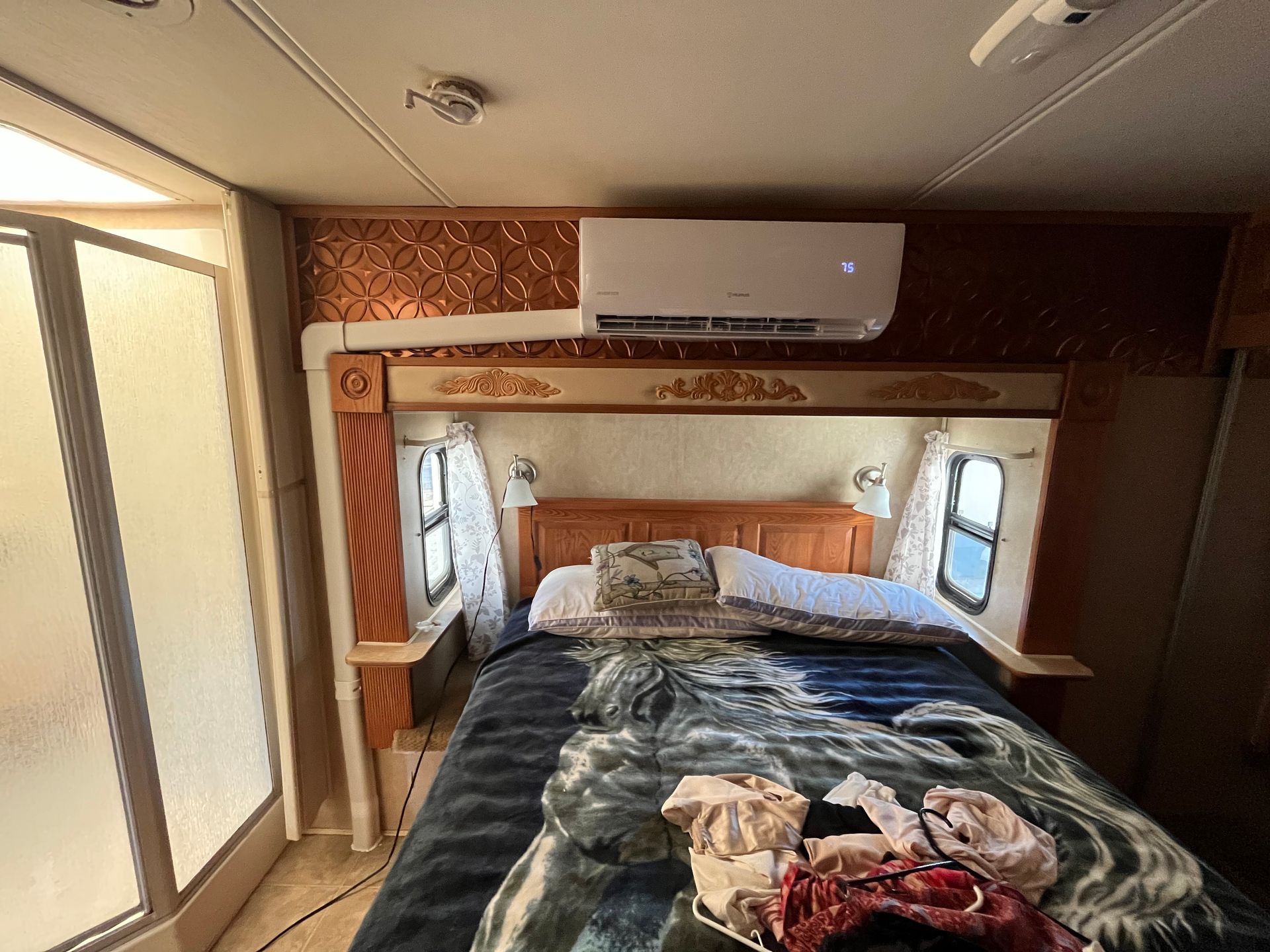 Bedroom in a RV with bed, air conditioner, shower, and windows.