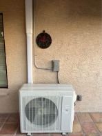 Outdoor AC unit against stucco wall, with electrical conduit and a decorative plaque.