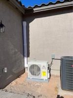 Outdoor HVAC units on a concrete pad next to a light-colored stucco building and downspout.