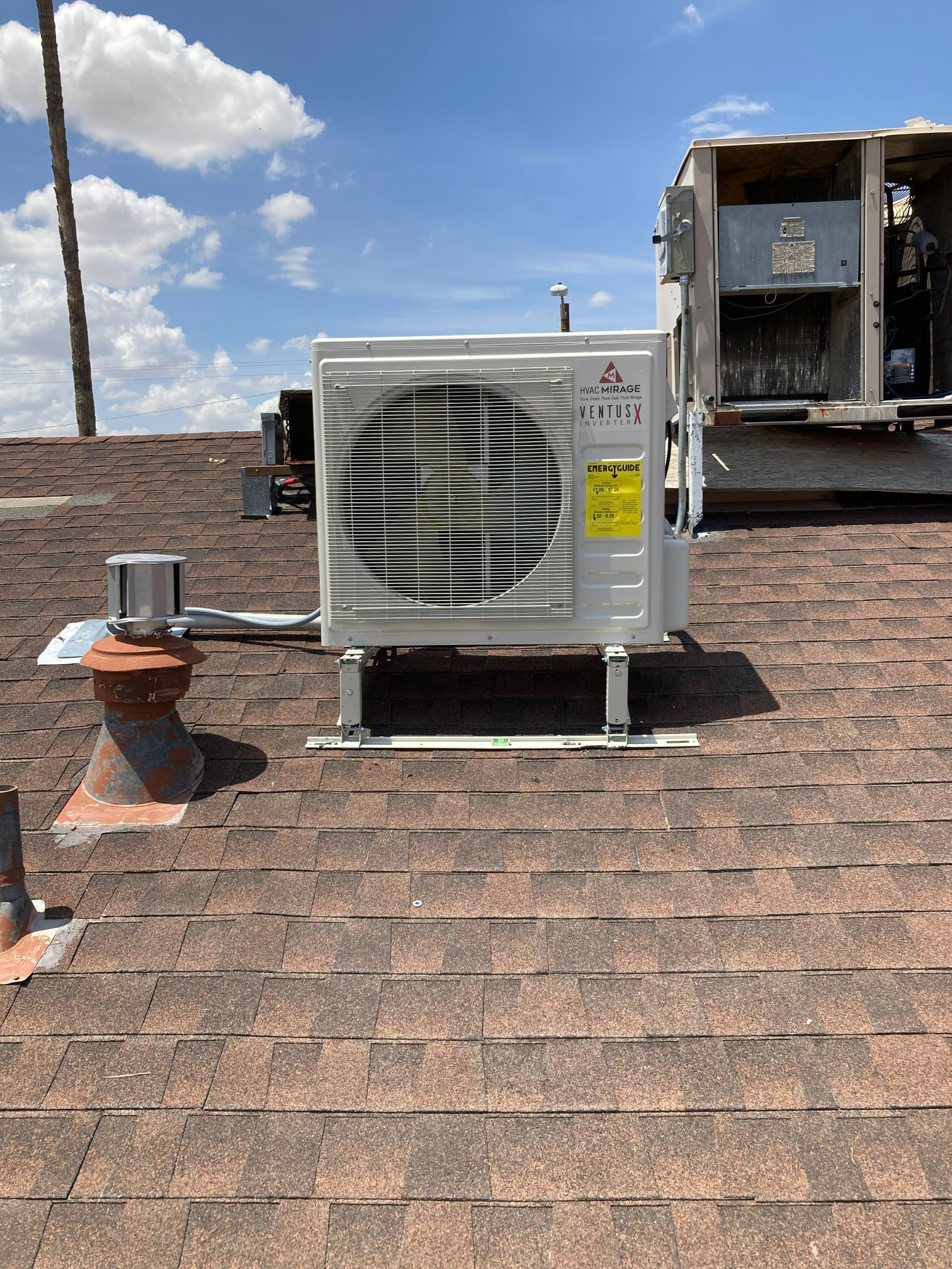 White Mitsubishi AC unit on a rooftop with shingles and a blue sky.
