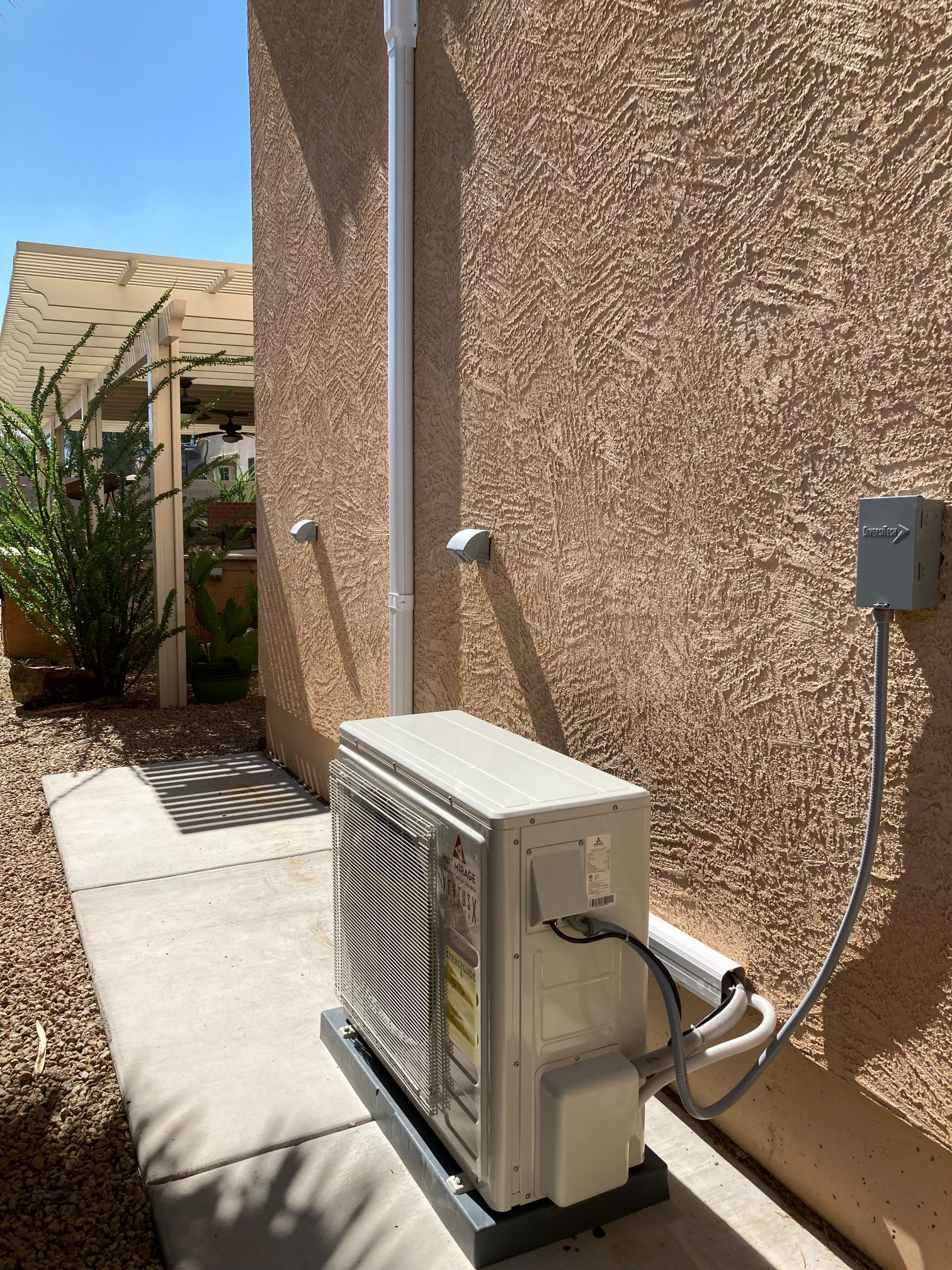 Outdoor air conditioning unit against a stucco wall, with electrical conduit and a concrete pad.