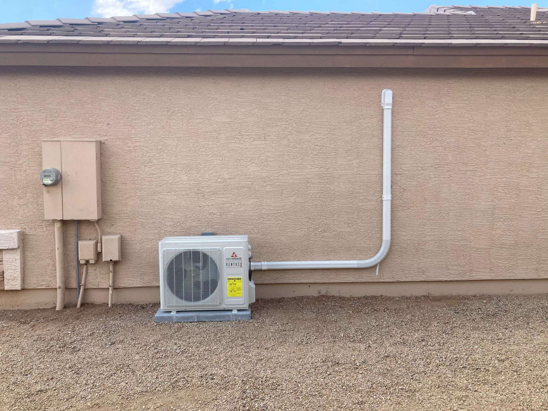 An air conditioning unit and electrical box are mounted on a stucco wall outside a building.