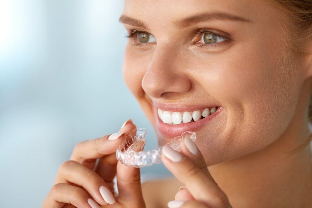 A Woman is Smiling While Holding a Clear Retainer — Ballina Denture Clinic Michael J Parker in Lismore, NSW