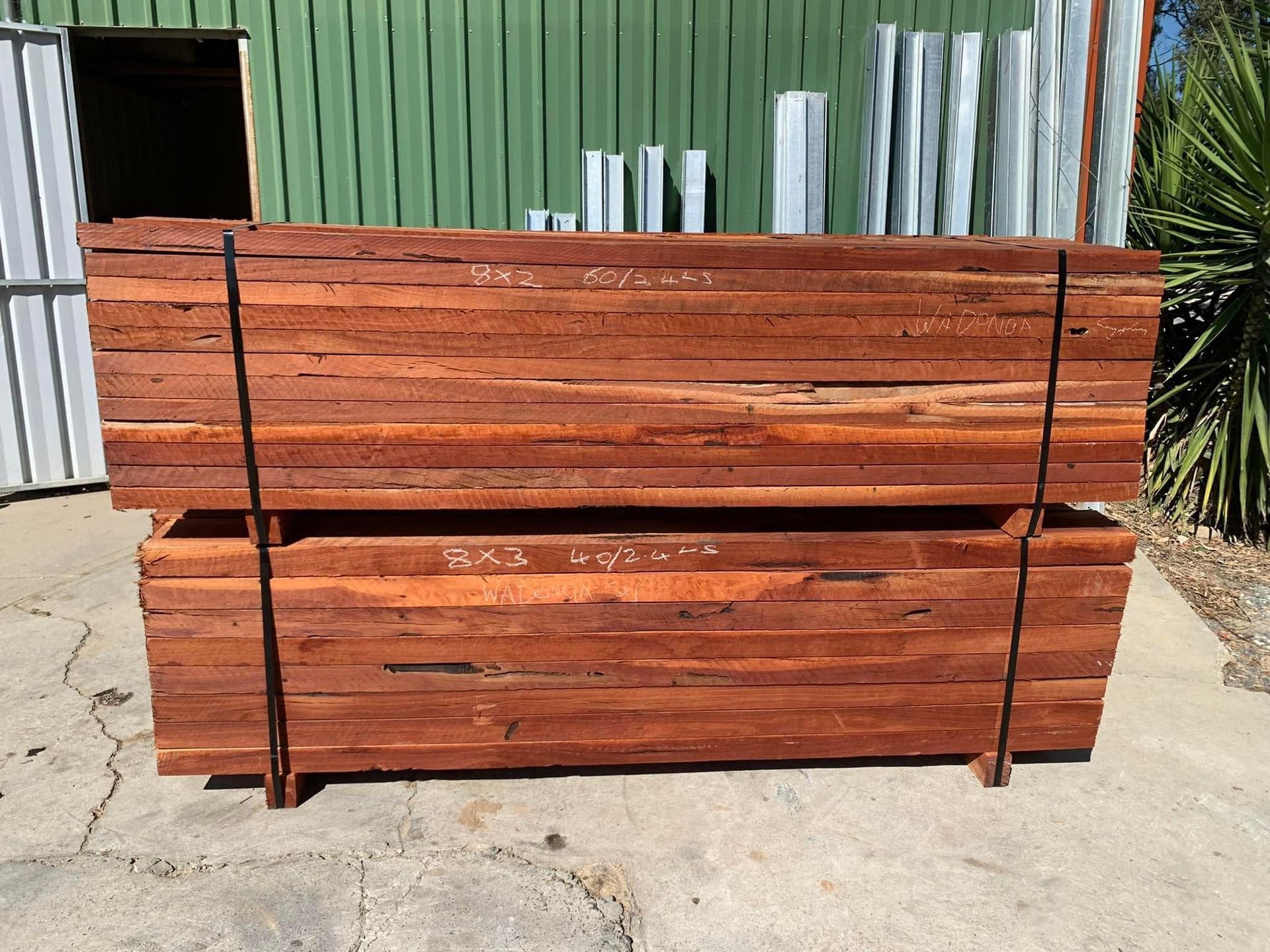 Two stacks of reddish-brown timber boards secured with black straps outside a green building. — Wodonga Sand & Soil in Wodonga, VIC