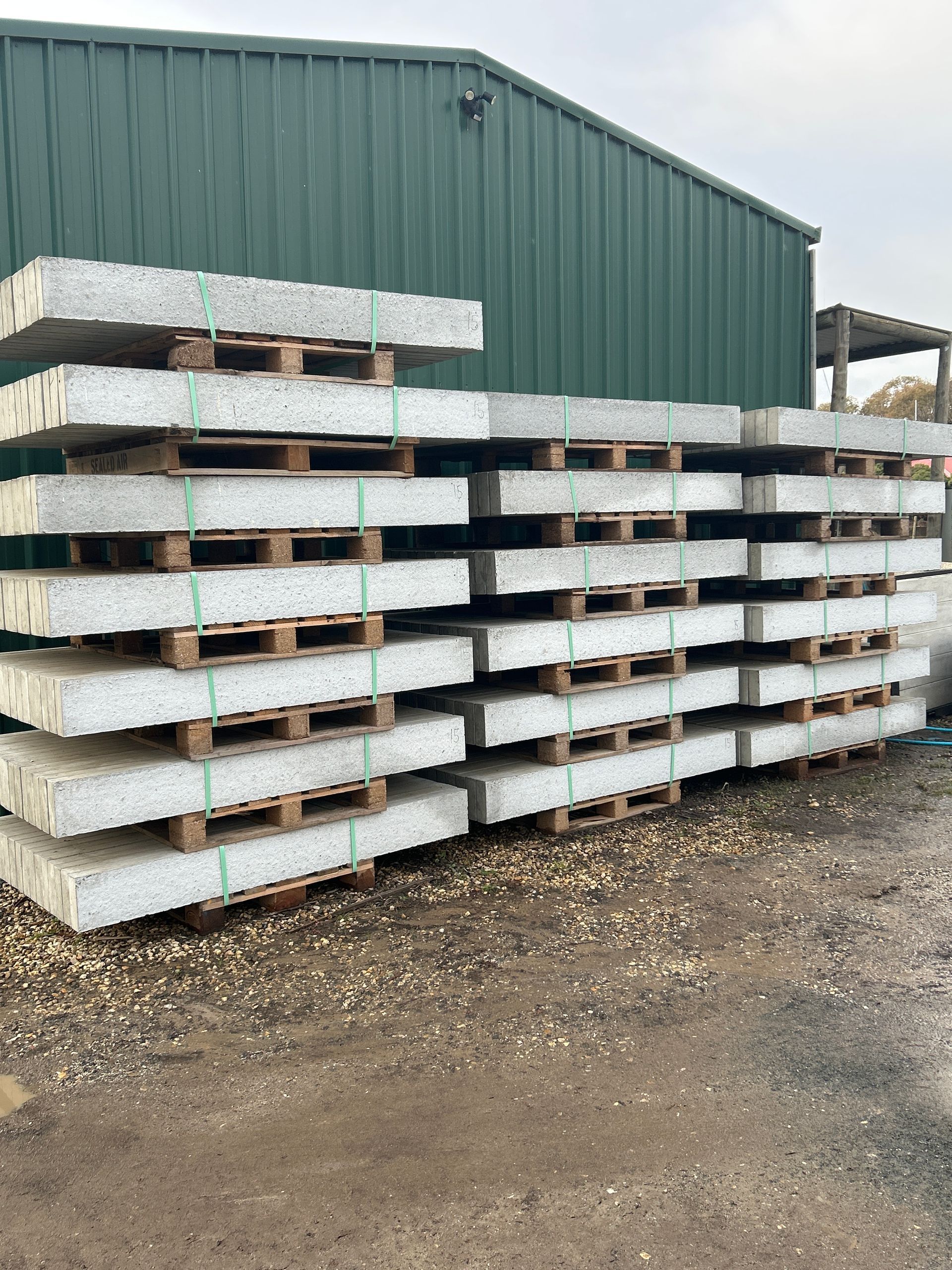 Pallets of gray concrete slabs stacked outside a green building. — Wodonga Sand & Soil in Wodonga, VIC