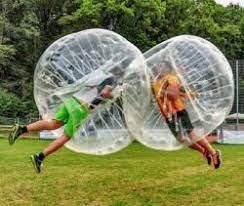 Two people in inflatable bubble suits collide mid-air above a grassy field.