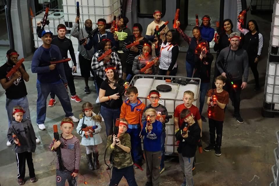 A diverse group of people in an indoor arena holding laser tag equipment, posed together for a photo.