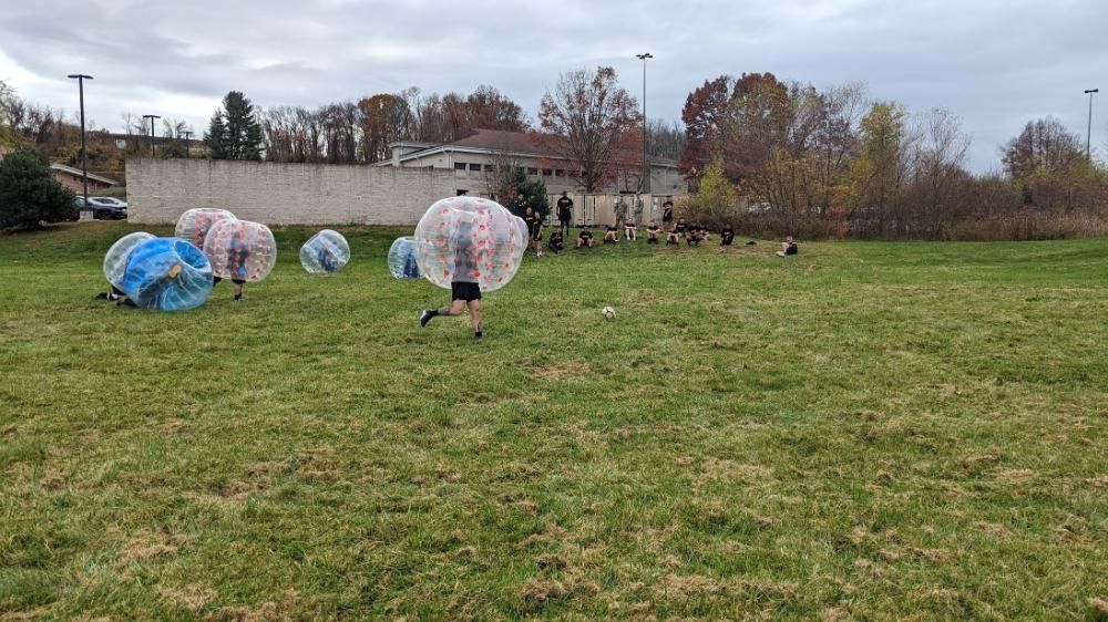 People playing bubble soccer on a grass field under an overcast sky.