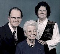 Three people posing for a portrait, with an elderly woman seated in front and two adults standing behind her.