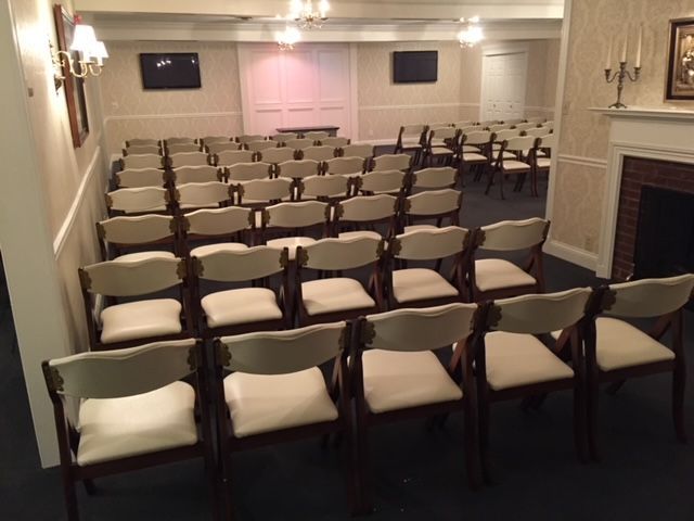Small auditorium with rows of empty white chairs facing a stage and pink backdrop