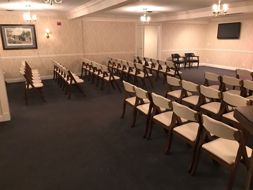 Empty conference room with rows of white chairs and dark carpet, lit by ceiling lights
