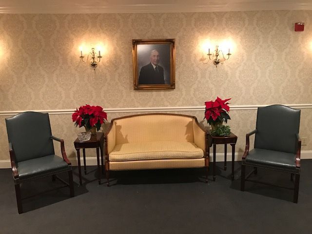 Elegant waiting room with cream sofa, two green chairs, side tables with red poinsettias, and a framed portrait on the wall