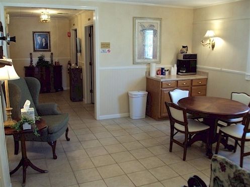 Cozy dining room with round table, chairs, sideboard, lamp, and tiled floor, opening to a hallway