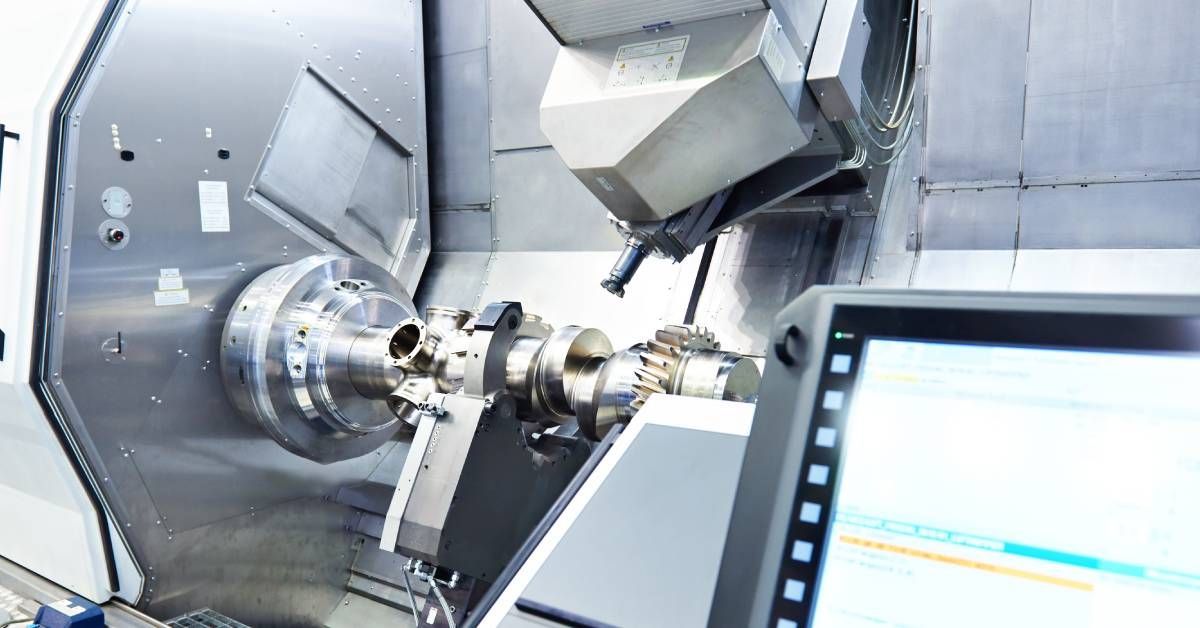 A screen on a CNC lathe in a factory with text and highlighting on the screen and a part being machined behind it.