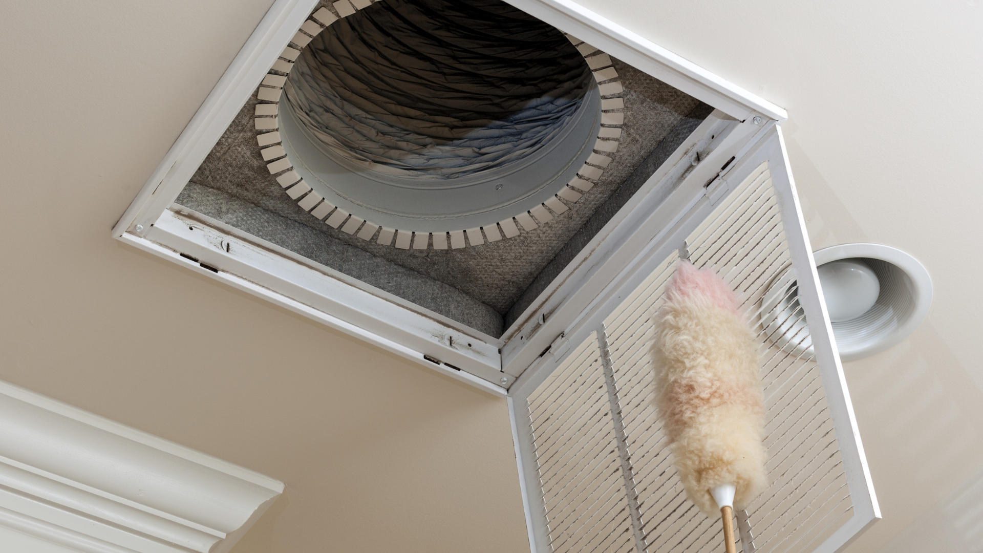 Ceiling vent being dusted with a pink feather duster. The vent is square, with a visible duct opening.