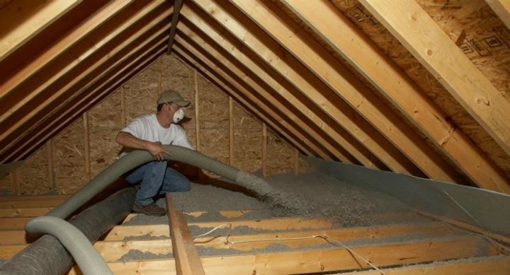A man is blowing insulation into the attic of a house.