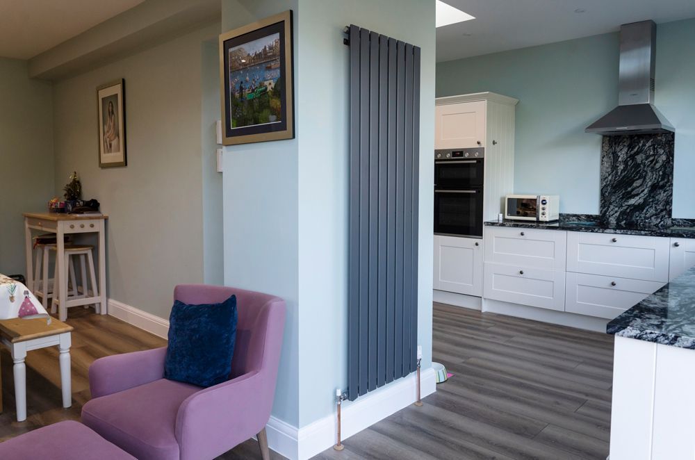 A living room with a purple chair and a kitchen with white cabinets in a Retrofit Consultancy in Rye