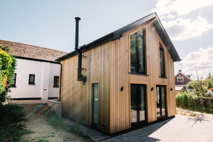 A house with a brick wall and a white roof is sitting on top of a lush green hillside  in East Sussex Passivhaus in Hastings