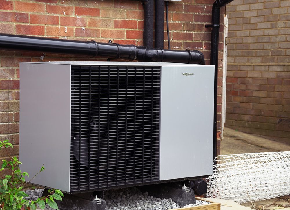 A large air conditioner is sitting outside of a brick building  in a Large-Scale Retrofitting in East Sussex