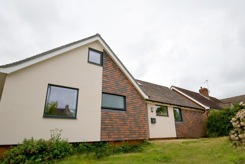A house with a brick wall and a white roof is sitting on top of a lush green field  in a Retrofit Consultancy in East Sussex