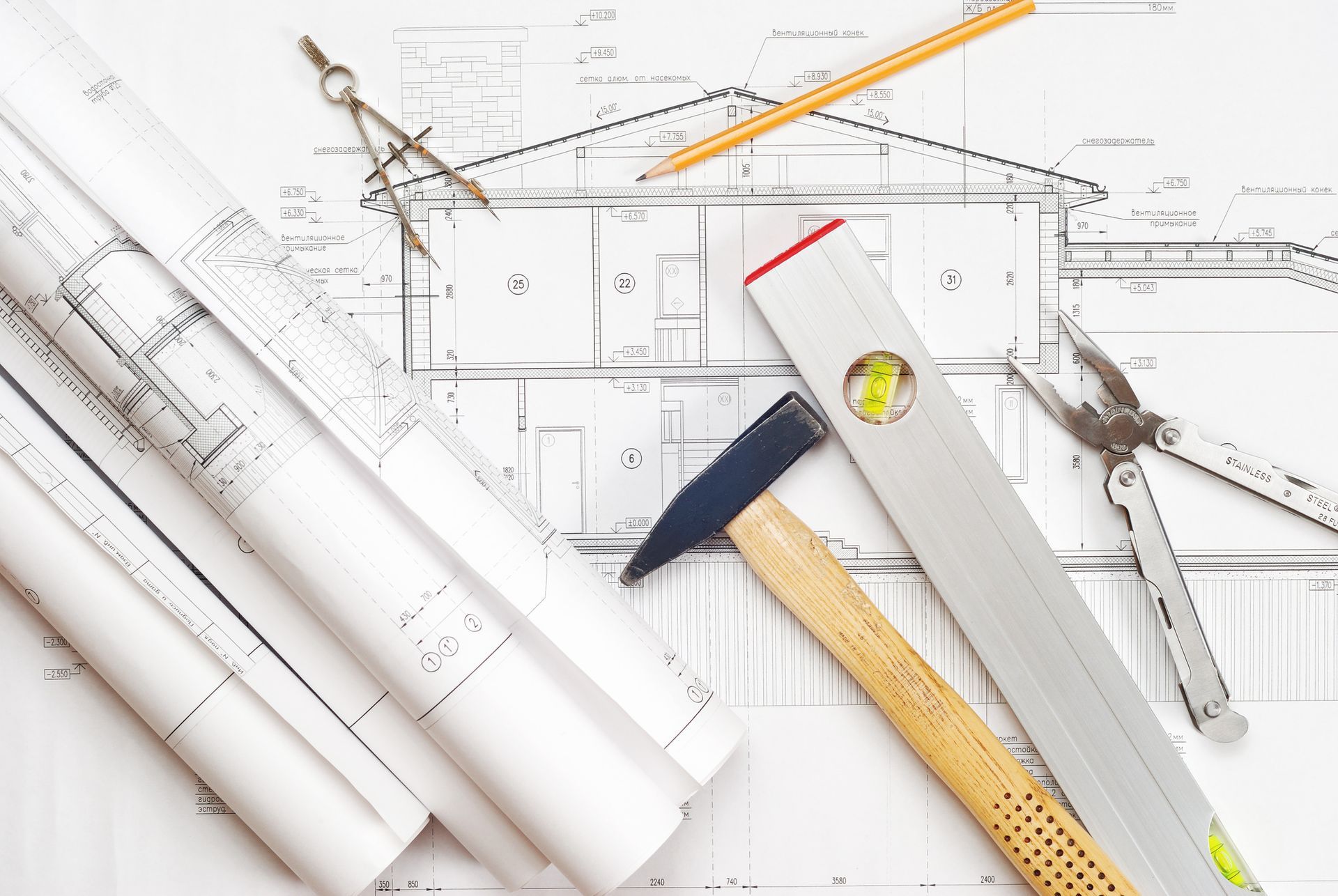 A Hammer , Level , Pliers , Compass and Pencil on Top of A Blueprint