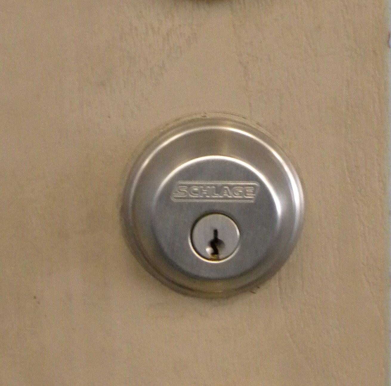 Close-up of a silver Schlage deadbolt lock installed on a beige door.