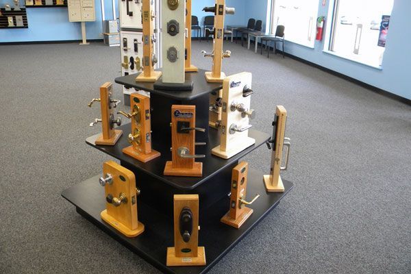 Display stand in Charm's Security locksmith shop filled with assorted door handles and locksets mounted on wooden blocks, arranged in tiers inside a showroom.